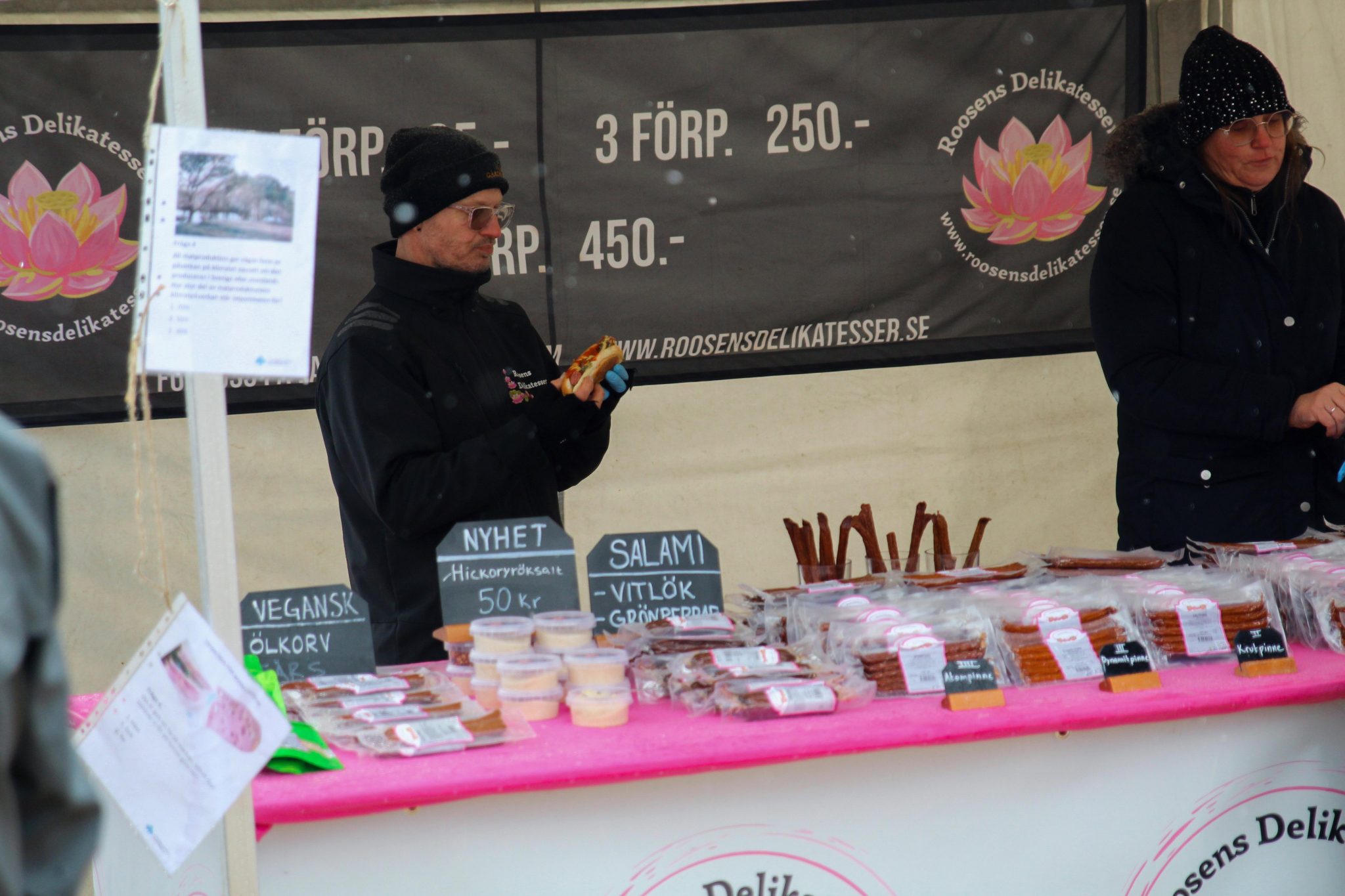 En utställare som säljer korv på ett rosa bord