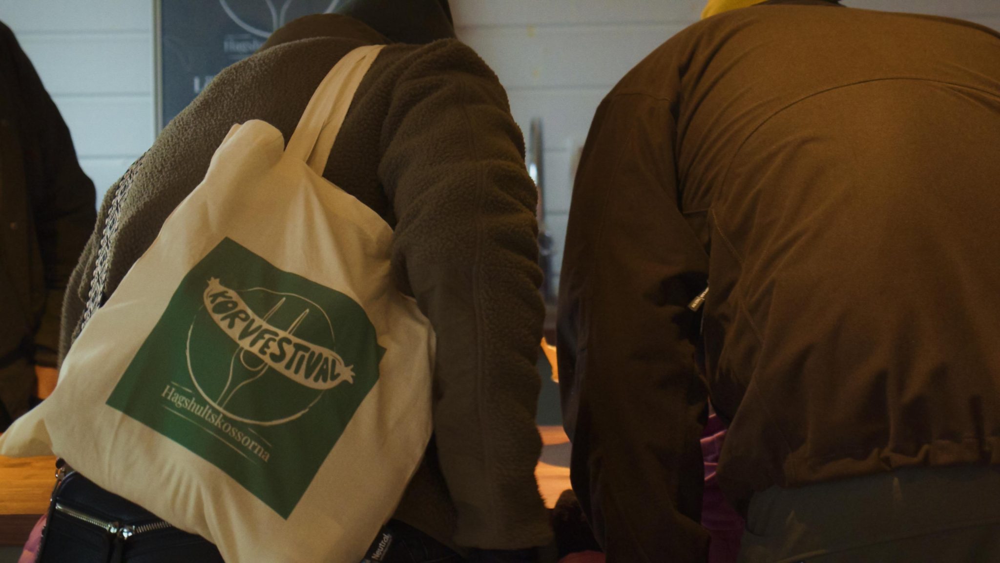 Två personer med ryggen mot kameran och en av de har en tygpåse över axeln